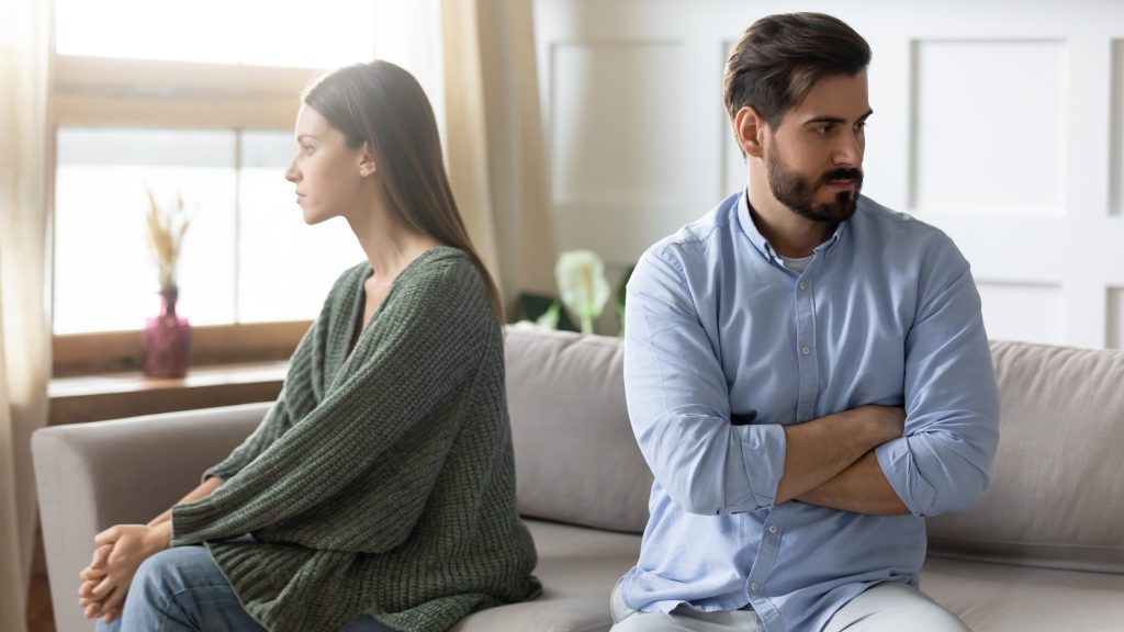 Wütendes junges Paar sitzt getrennt auf dem Sofa und ignoriert sich gegenseitig .