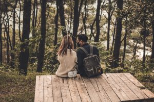 Ein Mann und eine Frau sitzen dicht nebeneinander. Sie befinden sich im Wald.