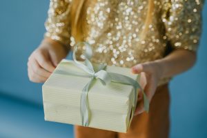 Eine Frau hält ein Geschenk in der Hand. Das Geschenk ist in weissem Papier und einer grünen Schleife eingepackt.